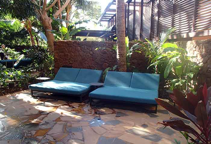 Big, cushioned lounges are surrounded by lush vegetation at Laniwai Spa's outdoor garden.